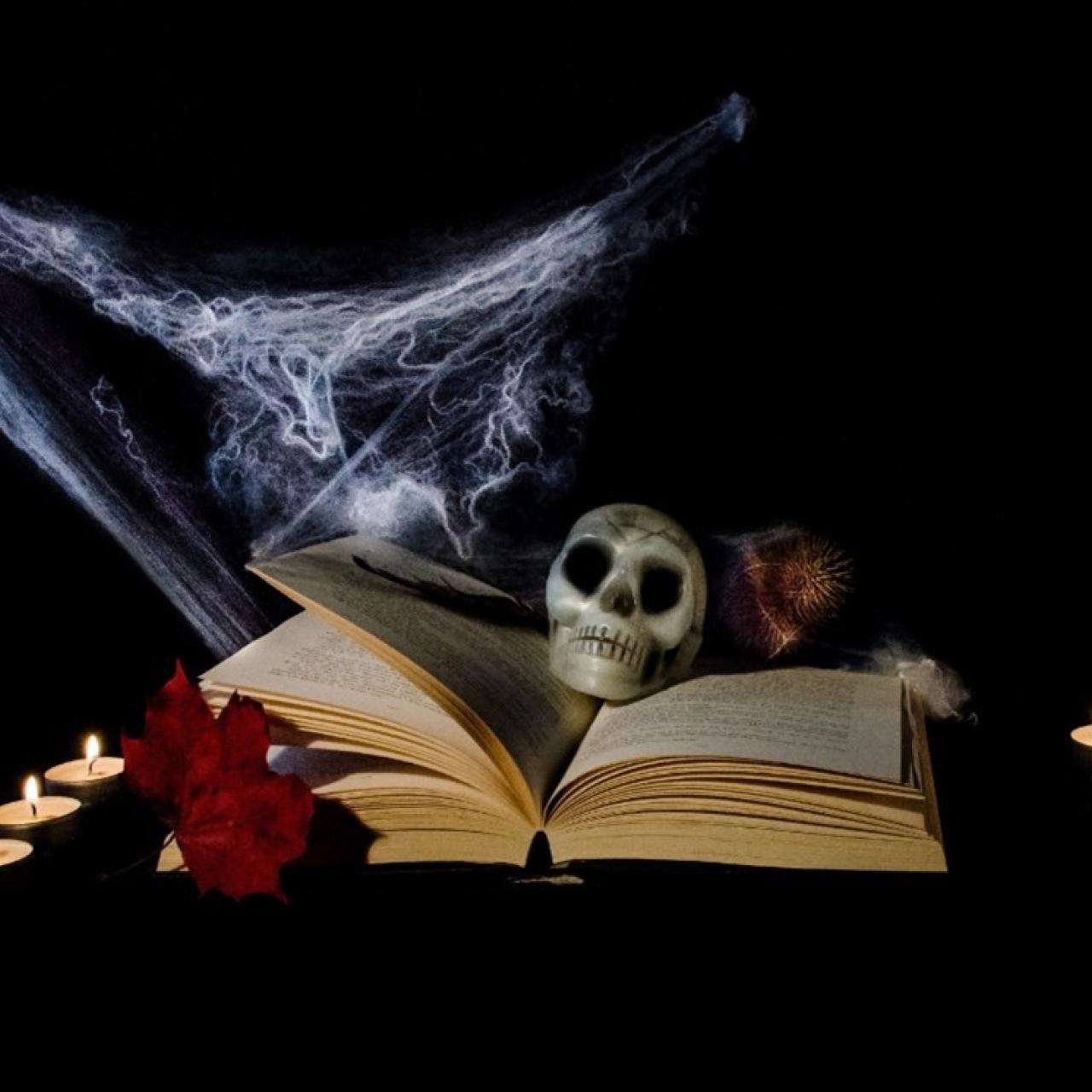 Aufgeschlagenes Buch mit Totenschädel, Spinnweben und von Kerzen umgeben